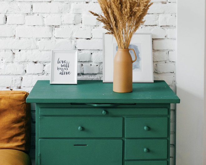 green chest of drawers with a vase and photo frames on top.